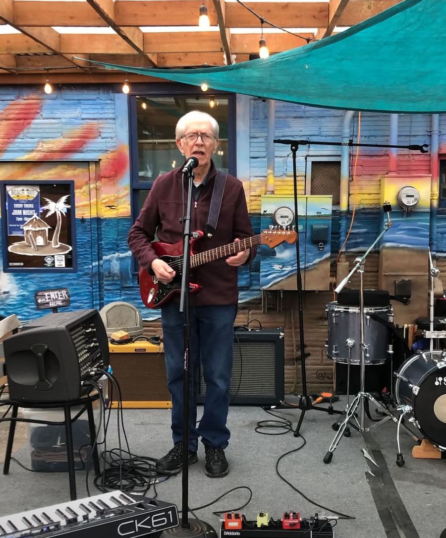 Dan Hess singing with a red electric guitar under the patio canopy at Beach Hut Deli